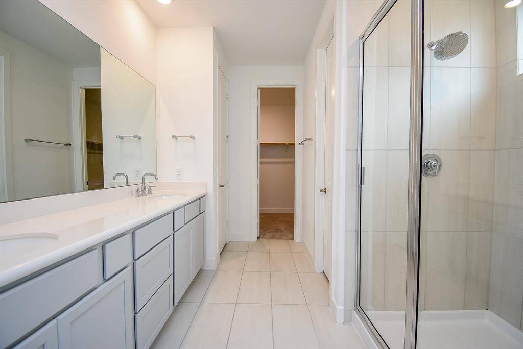 Luxurious primary bathroom featuring a sleek double vanity, spacious glass-enclosed shower, and elegant tile flooring.