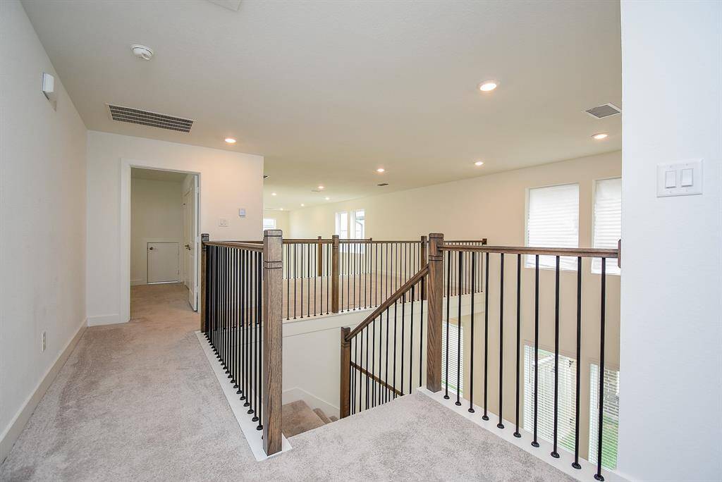 Bright and spacious upstairs landing with carpeted flooring and modern railing. Features recessed lighting, large windows for natural light, and access to additional rooms. Perfect for a family area or study nook.