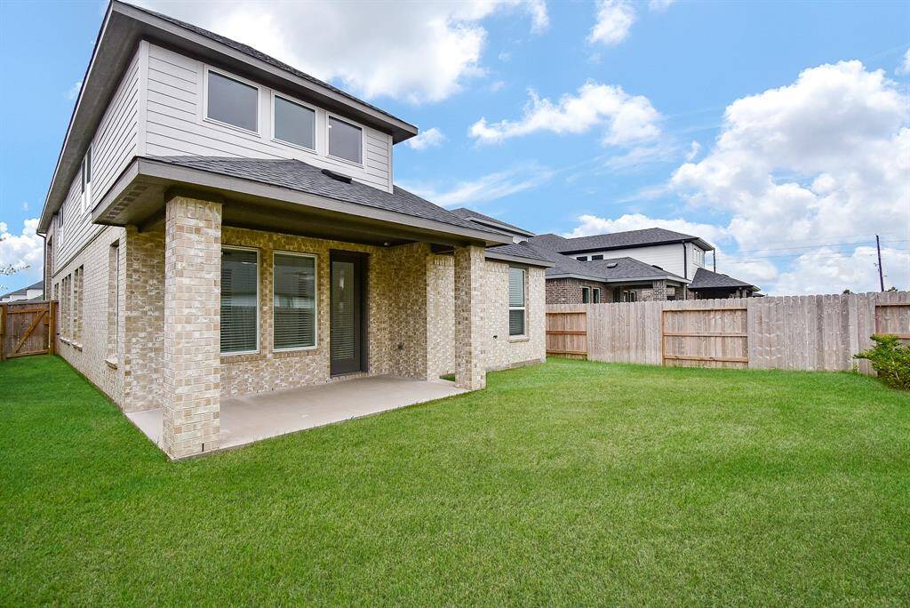 This photo showcases a modern two-story home with a brick exterior, featuring a spacious backyard with a well-maintained lawn. The covered patio provides a nice outdoor living space, and the fenced yard ensures privacy.