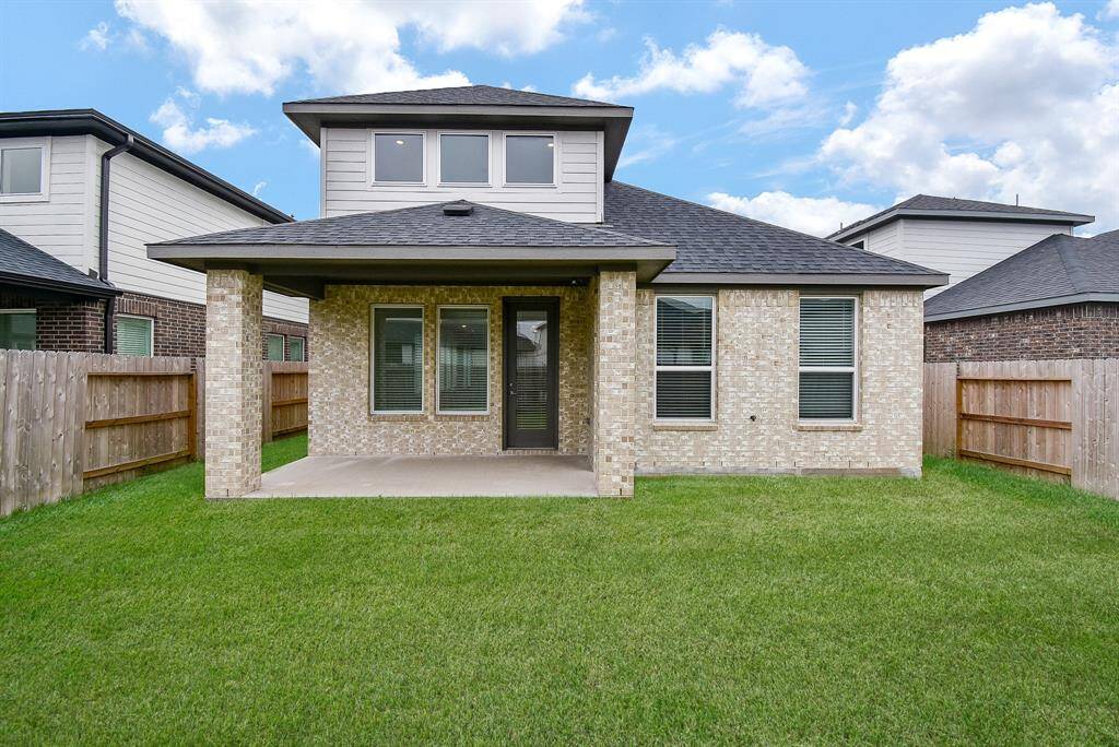 This photo showcases the back of a modern two-story home with a brick exterior, a covered patio, and a well-maintained fenced yard. Ideal for outdoor relaxation and entertaining.