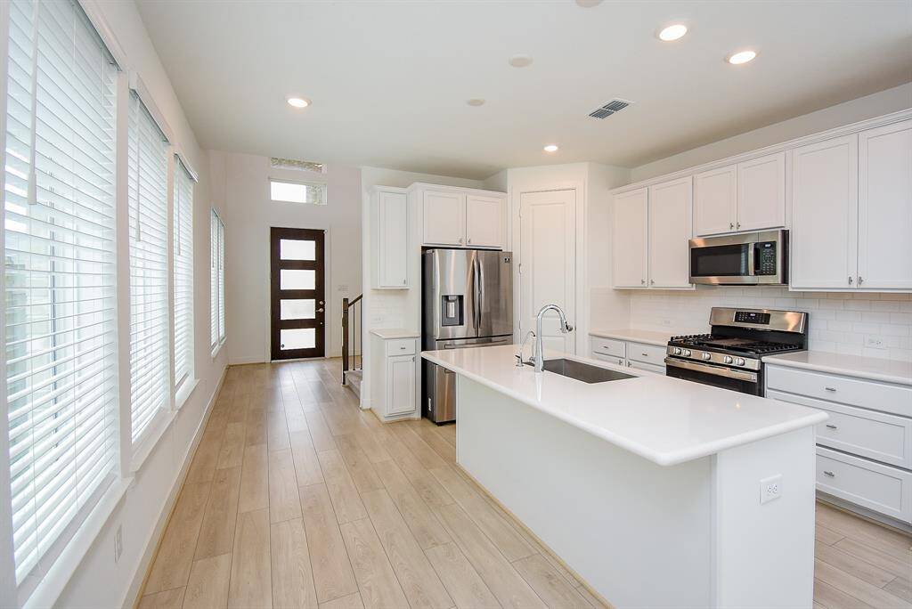 This photo showcases a modern, bright kitchen with white cabinetry, stainless steel appliances, and a large island. The space features light wood flooring and ample natural light from large windows, creating an inviting and airy atmosphere.
