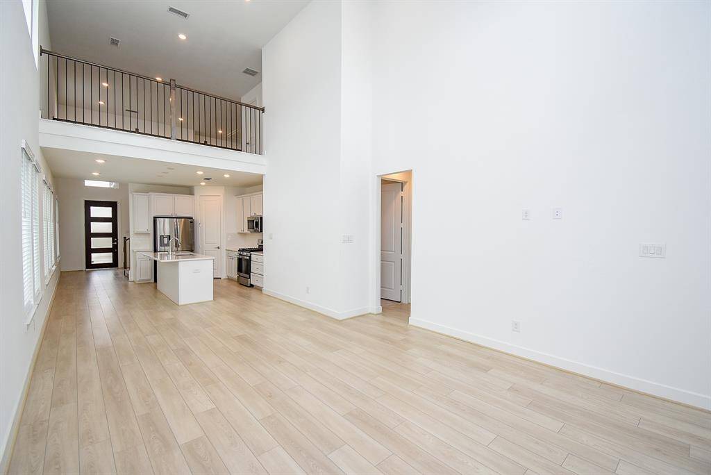 Spacious, modern open-concept living area with high ceilings, light wood flooring, and abundant natural light. Features a sleek kitchen with stainless steel appliances and an upstairs loft area.