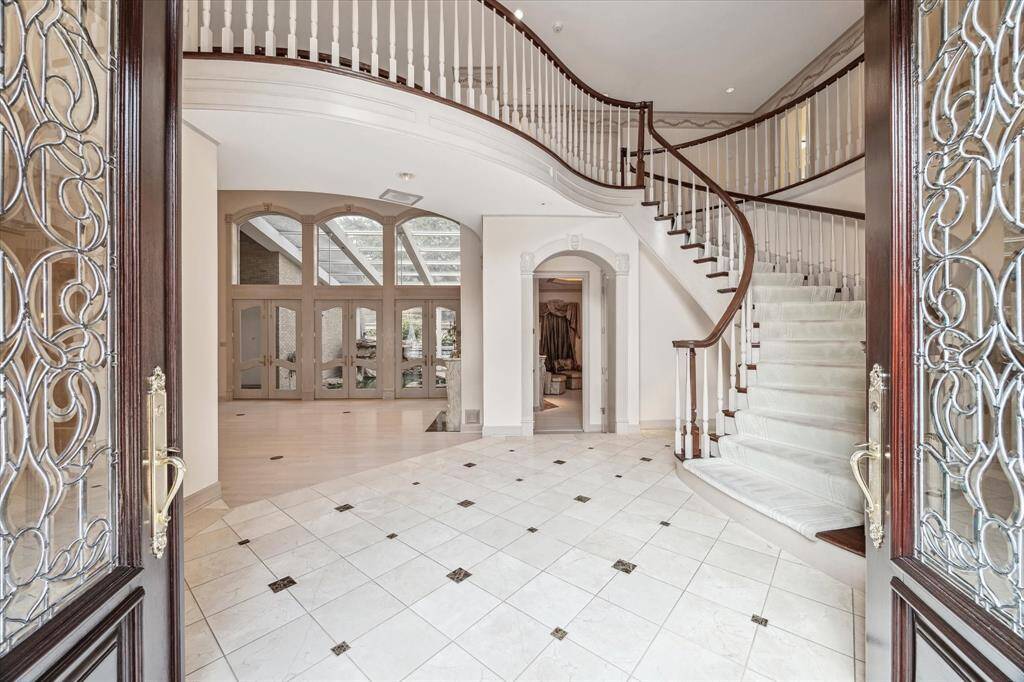 This grand entrance features an elegant spiral staircase, ornate glass doors, and a spacious, marble foyer with high ceilings, offering a luxurious first impression.