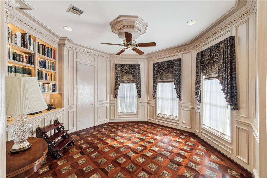 This elegant room features Randy Yost hardwood/marble flooring with a geometric pattern, built-in bookshelves, and large windows adorned with luxurious drapery. The space is accented by detailed wood paneling, creating a sophisticated and inviting atmosphere. Ideal for a study or reading room.
