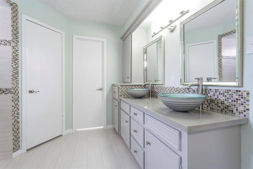 The spa-inspired vanity steals the show with a sleek quartz countertop, eye-catching decorator tile backsplash, and matching framed mirrors. Dual vessel sinks with modern faucets add a luxurious touch, making your morning routine feel like a trip to the spa.