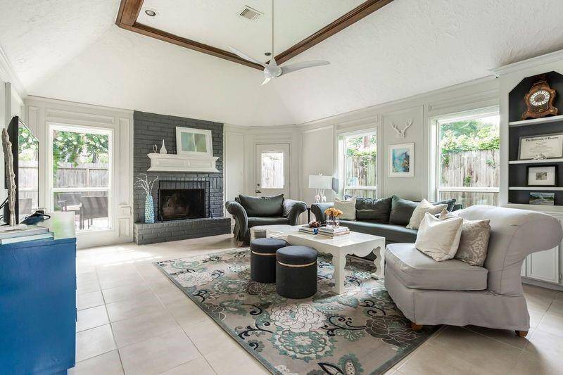 This light-filled family room is the heart of the home, featuring a cozy gas-log fireplace with a striking tile surround, custom built-ins, and durable tile flooring. Enjoy backyard views through scattered windows and a charming cottage-style door, perfect for both everyday living and effortless entertaining.