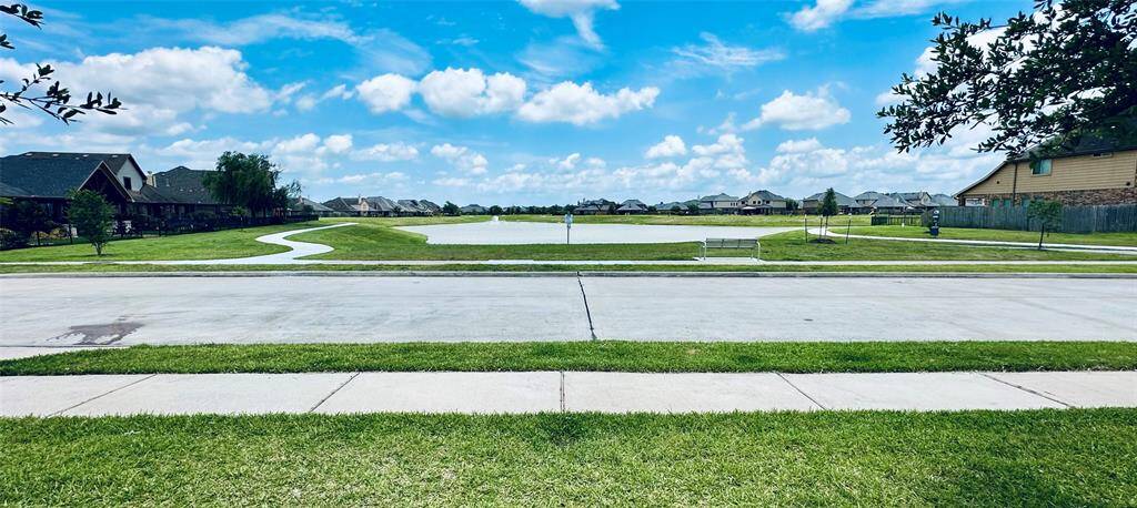 A serene neighborhood with a view of a pond and walking path from your home. The homes are well-spaced, and the area is landscaped with green grass and trees, offering a peaceful suburban setting. This is the view you will have every time you arrive and leave your home