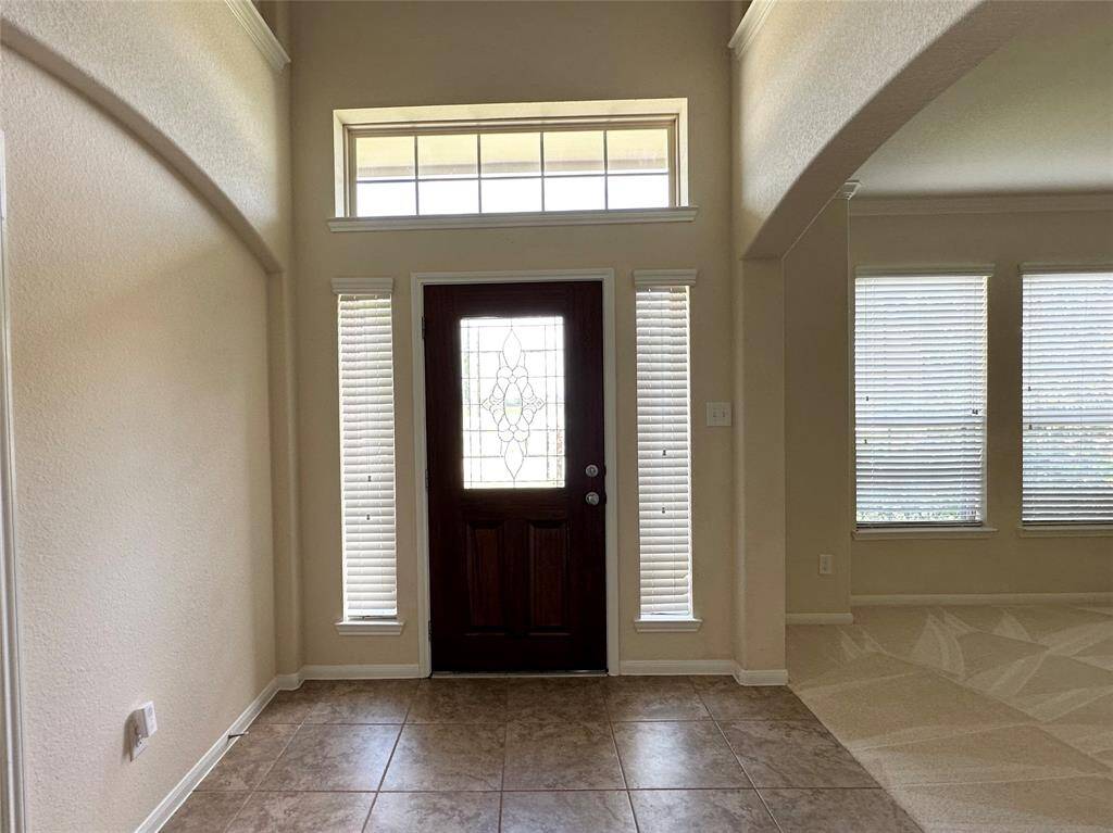 Welcoming entryway with a dark wood front door featuring decorative glass. The area has tile flooring, high ceilings, and ample natural light from transom and side windows, creating an inviting atmosphere.