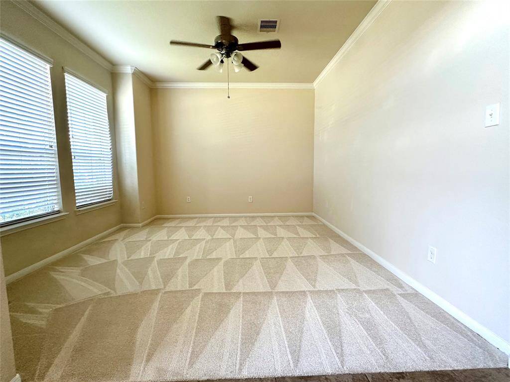 This room features neutral walls, a new carpet with a patterned vacuum finish, large windows with blinds for ample natural light, and a ceiling fan for added comfort. Perfect for a cozy dining area or office space.