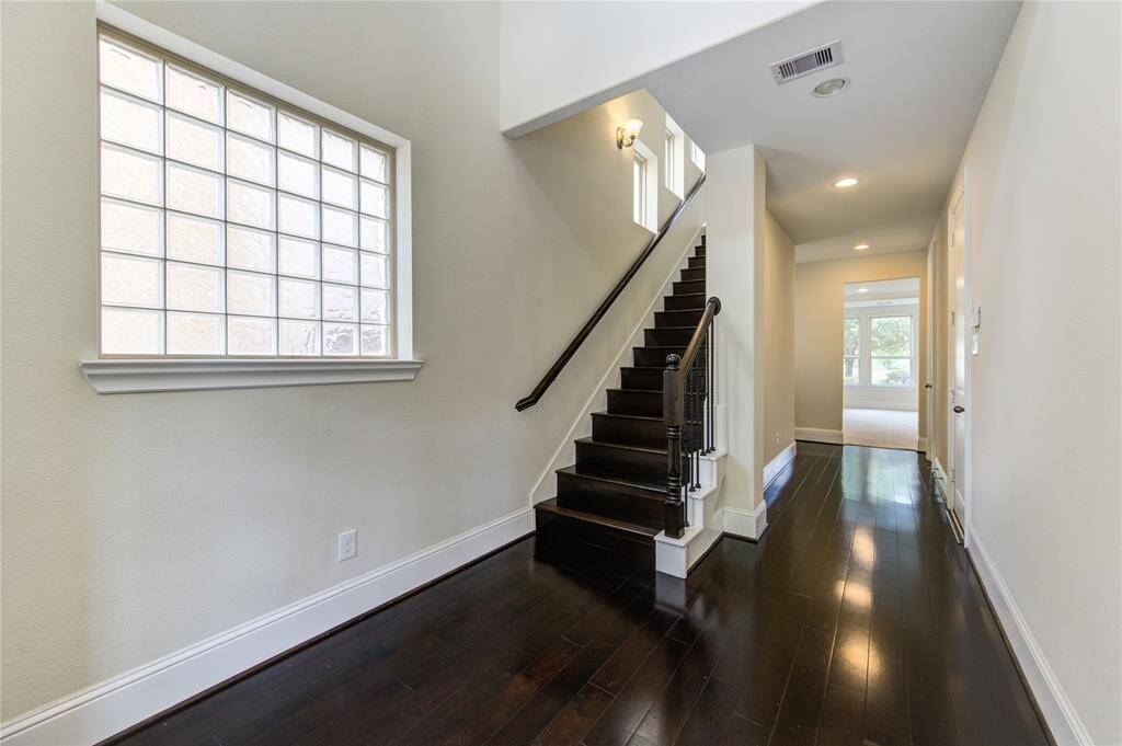 This entryway features dark hardwood floors and a staircase with a sleek railing. A large glass block window provides natural light, leading to a bright, open hallway.
