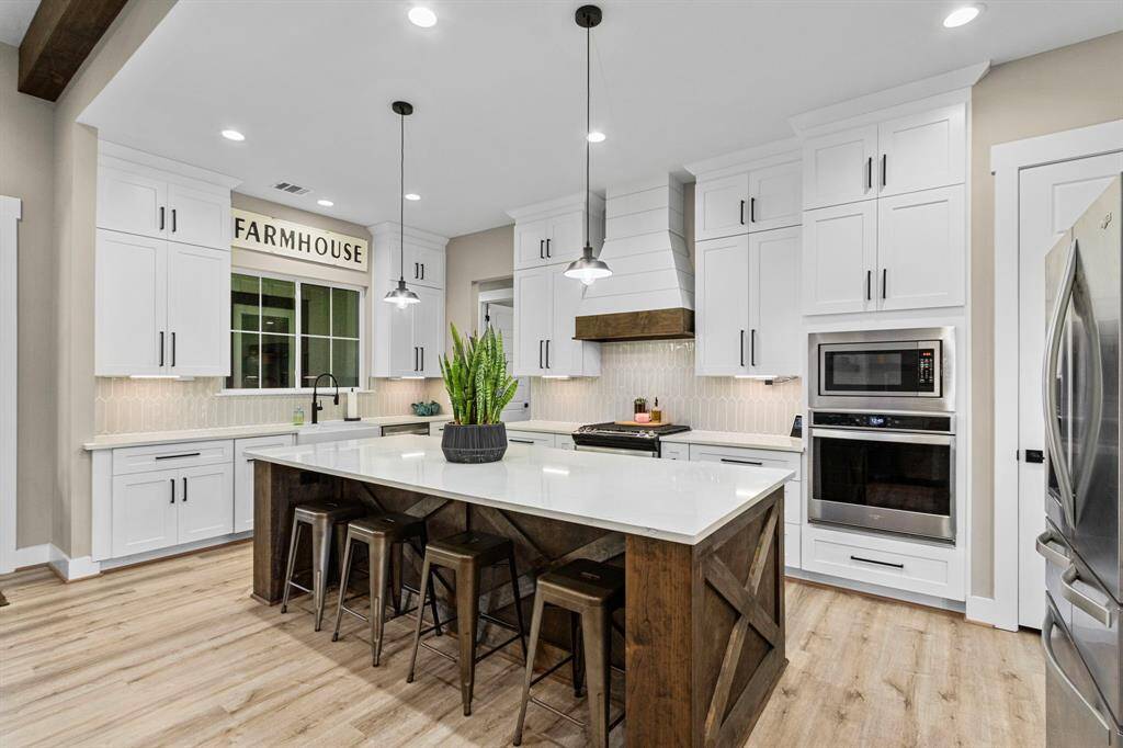 This custom oversized island has plenty of seating for family and friends, well lit with under cabinet lighting and overhead recessed and bar lights. You have a gas range and oven combo as well as an electric oven and microwave to the side.