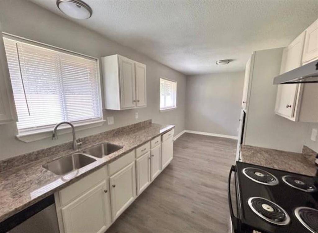 This kitchen features bright white cabinetry and granite countertops. It has neutral colors, with ample natural light, and laminate flooring throughout.