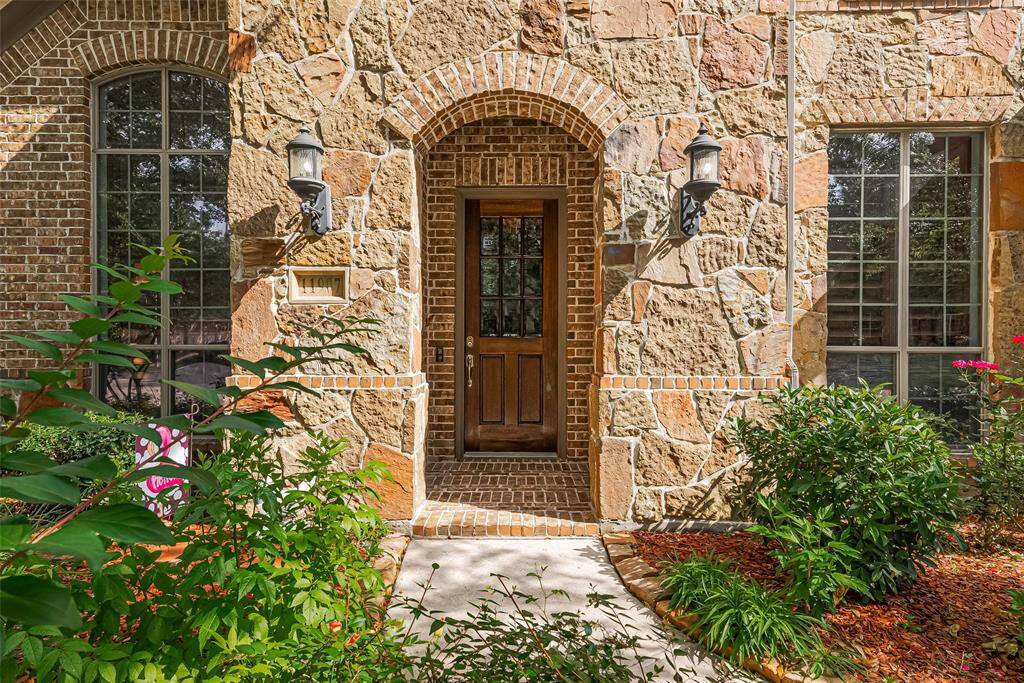 Inviting front entry framed by elegant stonework, twin sconces, and manicured garden beds for a warm first impression.
