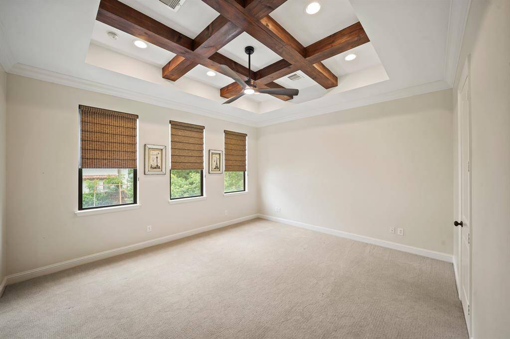 The owner's suite with crown moulding includes a beautiful recessed & wood beamed coffered ceiling with recessed lights, ceiling fan with lighting & patterned carpet.