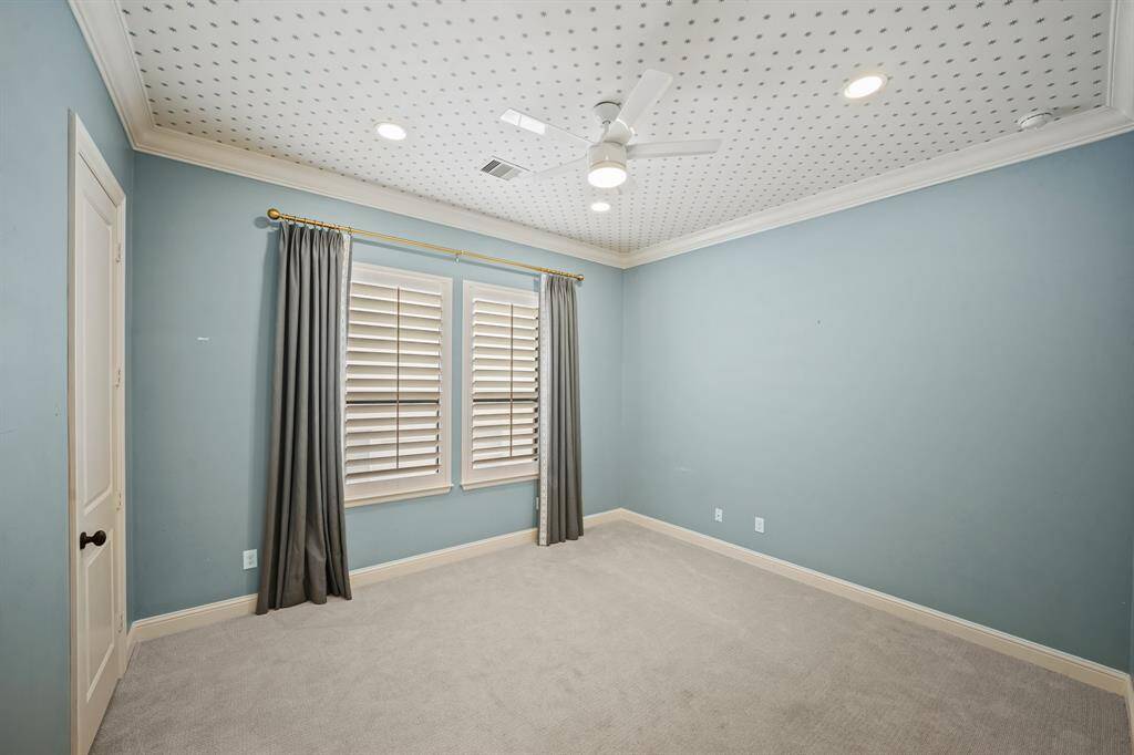 The secondary bedroom with semi-private access to the home's second full bath includes crown moulding, ceiling recessed lighting, a ceiling fan with light fixture, windows with drapes & plantation shutters and a wardrobe closet.