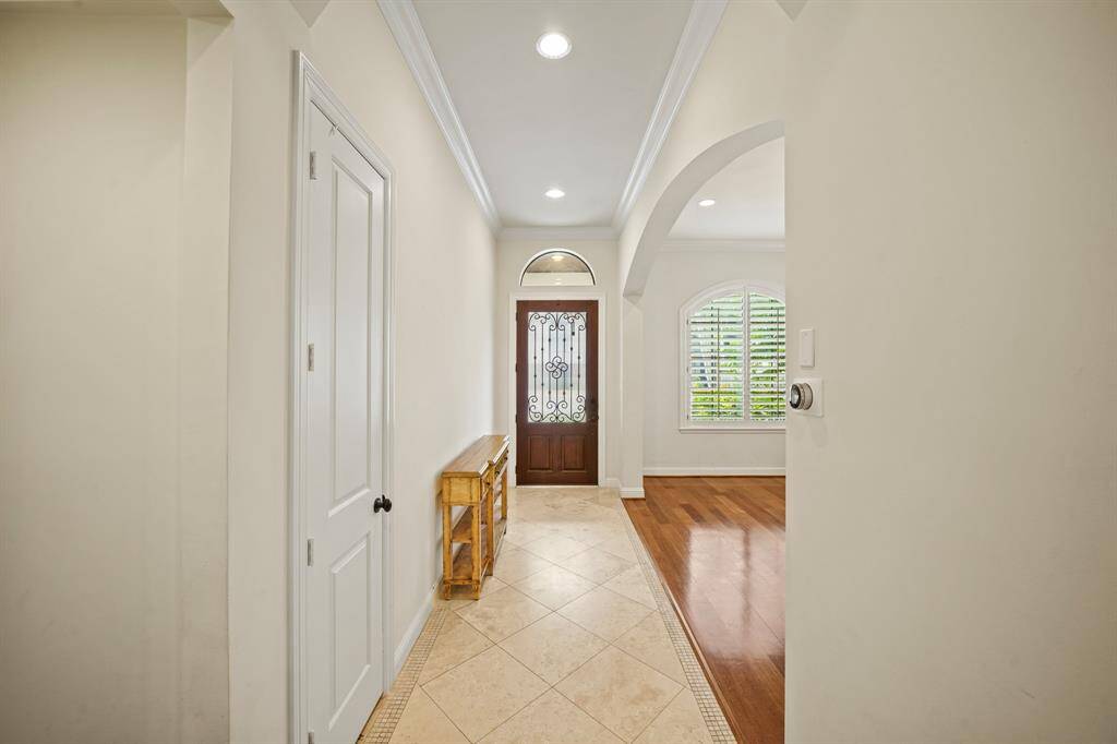 The foyer of the home features a high ceiling with crown moulding, recessed lighting, space for accent furniture, a coat closet and diagonally-laid travertine tile flooring. Just to the right of the wood-stained & wrought iron entry door with privacy rain glass is an arched opening leading to the formal dining room.