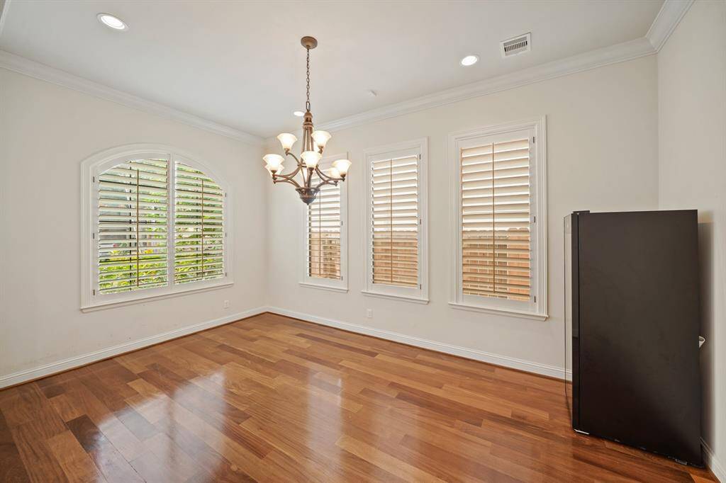 Surrounded by windows with plantation shutters, the formal dining room with crown moulding & recessed lighting includes a beautiful chandelier and gleaming wide-plank hardwood floors. The free-standing wine fridge is shownin the right corner will stay with the home.