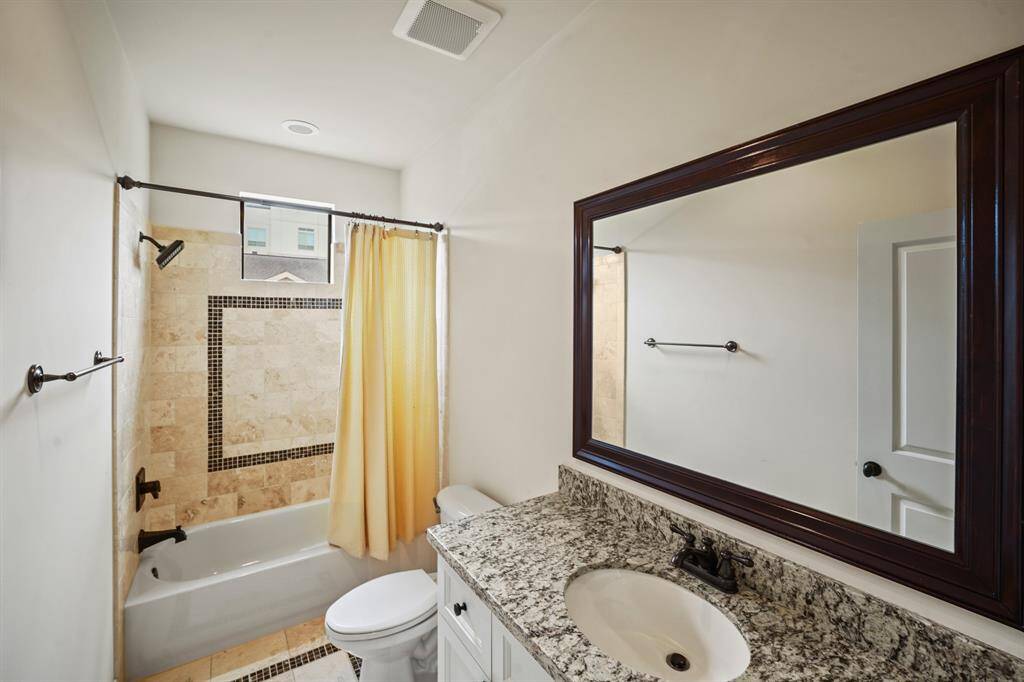 The fourth full bath has white painted cabinets with a granite counter, under-mount sink, custom framed mirror, tiled combination tub/shower & travertine flooring with decorative granite insets.