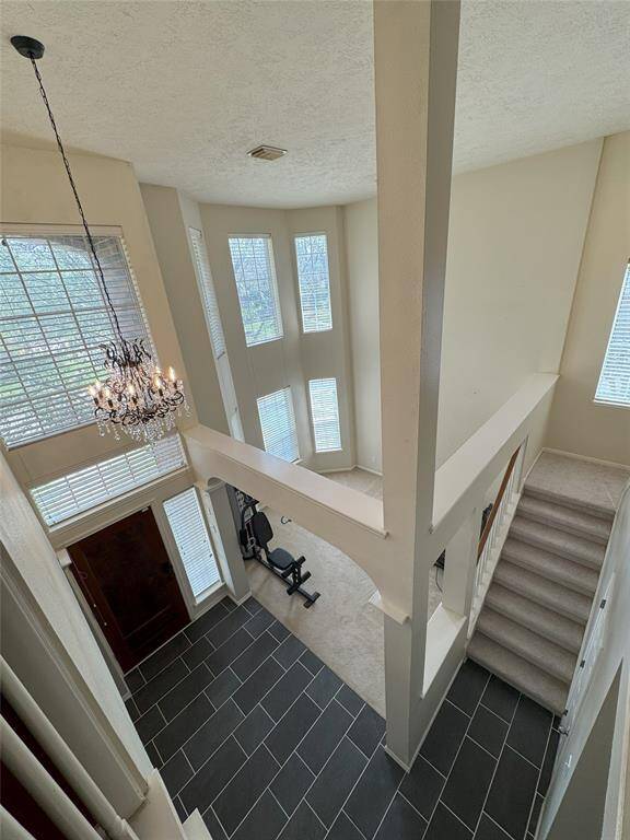 An aerial view of this breathtaking entryway highlights its dramatic high ceilings, oversized windows, and architectural details. The newly installed carpet on the stairs enhances both comfort and style, leading to the spacious second floor.