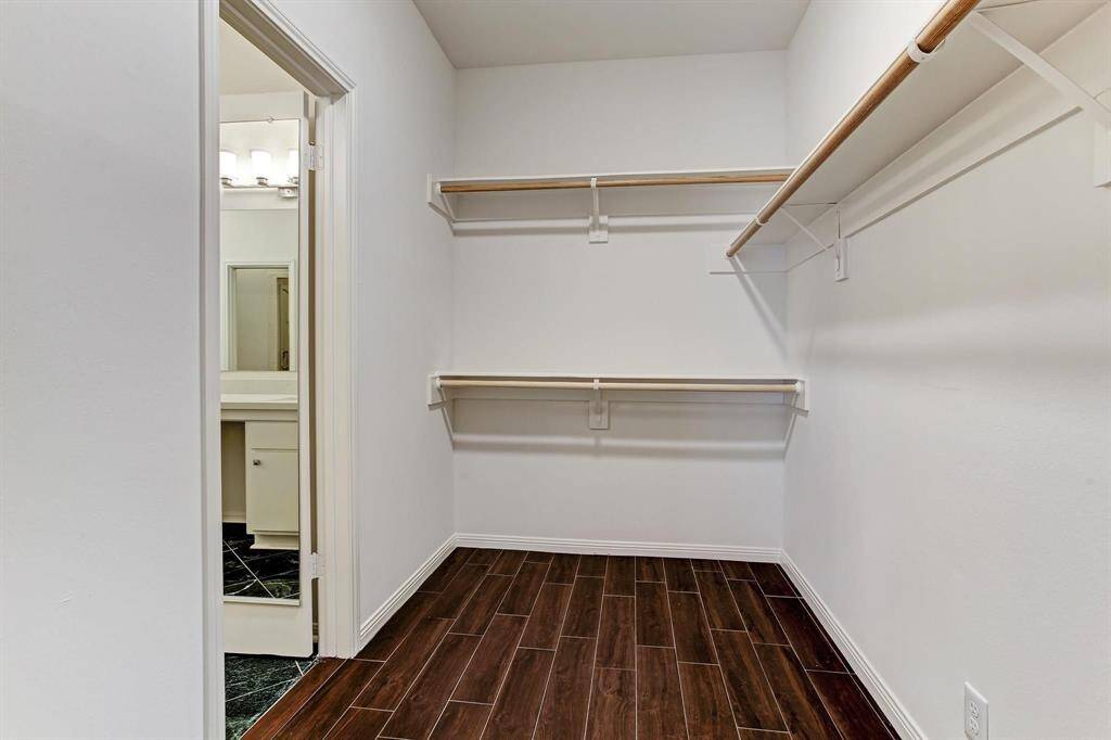 One of two large walk-in closets in the primary suite with wood-look porcelain tile floor.