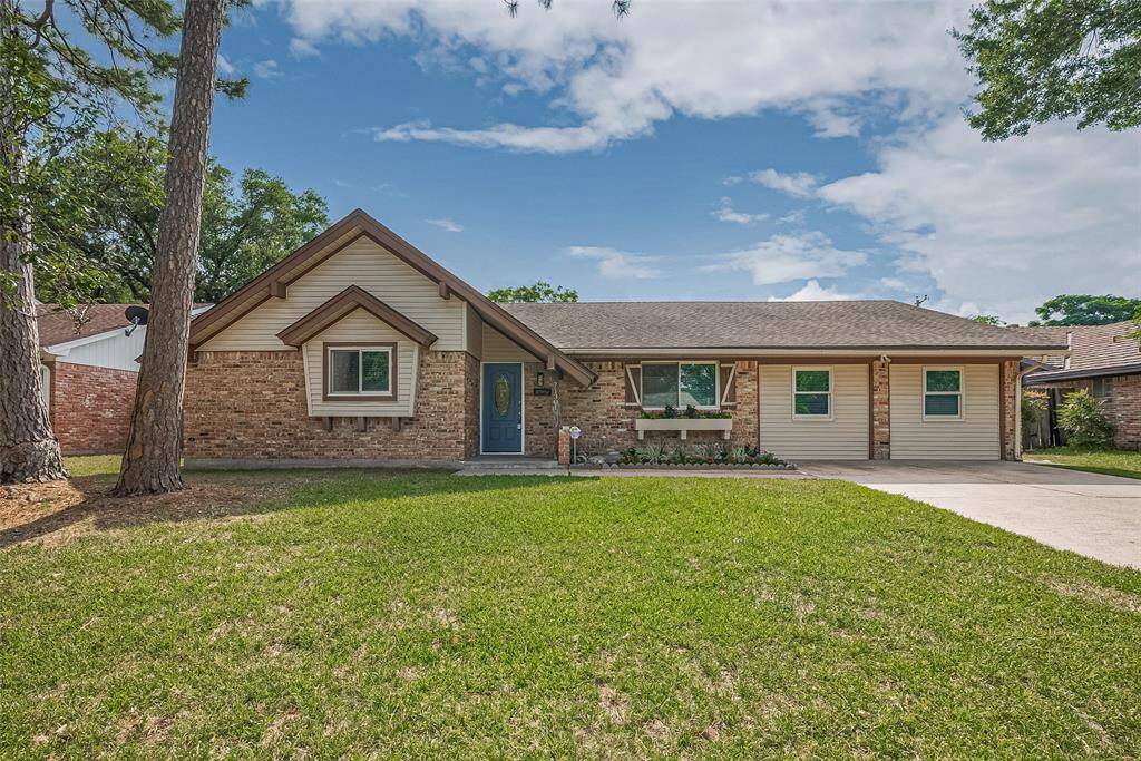 charming single-story brick home with a neatly maintained lawn and a spacious driveway. The house features a peaked roof with dormer windows and a welcoming front door. The surrounding trees add a cozy, natural ambiance to the property.