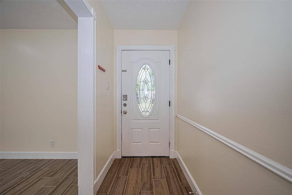 Entryway features a charming door, neutral walls, and brand-new wood- tile flooring, leading into a bright, inviting space.