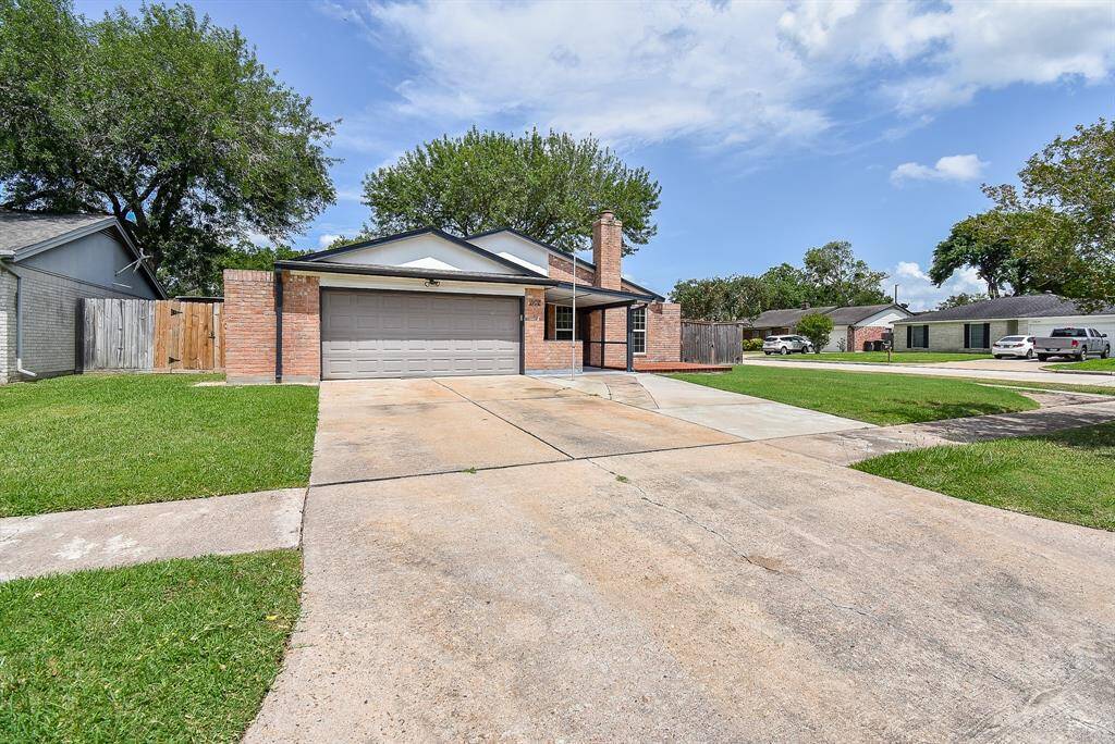 This photo shows a single-story brick home with a two-car garage and a spacious driveway. The front yard is well-maintained with a lawn, and the house is situated in a suburban neighborhood, offering a welcoming and tidy appearance.