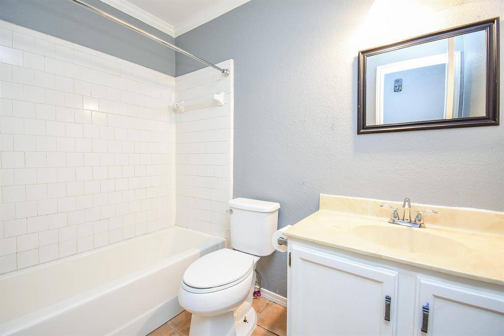 This bathroom features a classic design with a white tiled shower and tub combination. It has a sleek vanity with a light-colored countertop and a framed mirror above. The walls are painted a soft gray, offering a clean and modern look.