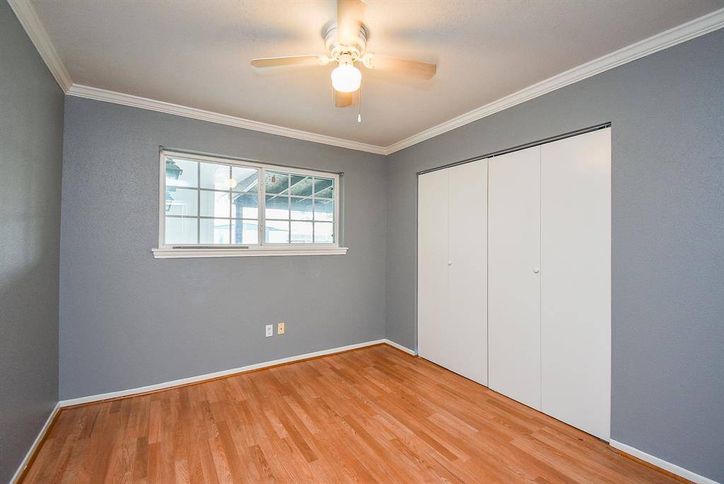 This room features hardwood floors, a ceiling fan, and neutral gray walls. It has a window for natural light and a spacious closet with white sliding doors, offering a clean and modern look.