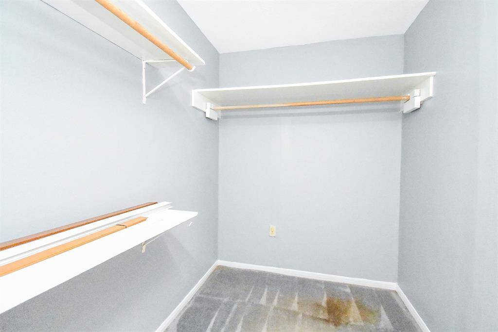 This is a spacious walk-in closet with light gray walls, featuring several white shelves and wooden hanging rods for ample storage. Perfect for organizing clothes and accessories.