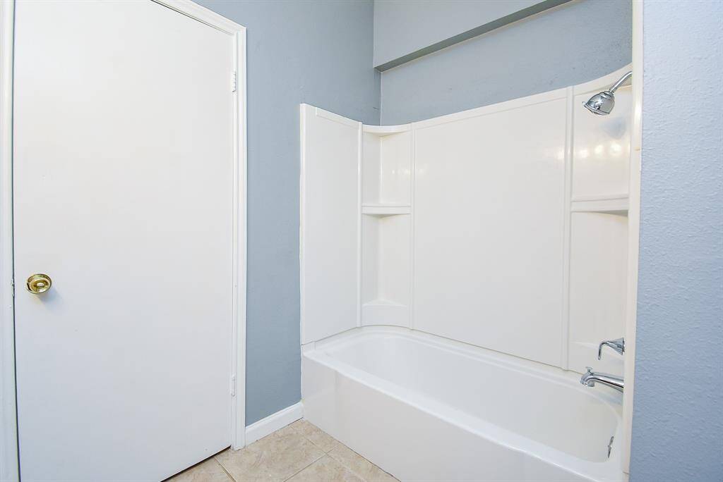 This bathroom features a clean, modern design with a white bathtub and shower combo, light gray walls, and tile flooring. The space includes convenient built-in shelving for storage.