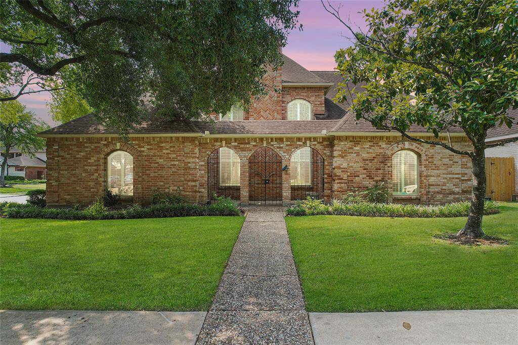 Welcoming arched entrance, surrounded by lush landscaping. The home sits on a corner lot, offering extra space and privacy.