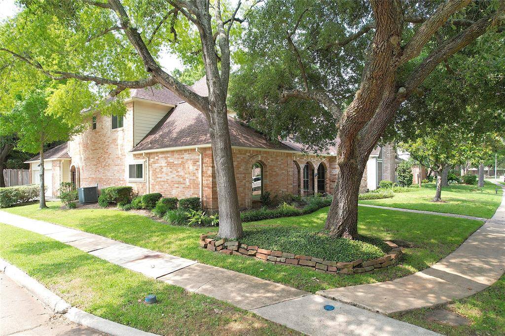 Charming brick home on a corner lot with mature trees and well-maintained landscaping. Features a two-story design, arched windows, and a cozy sidewalk leading to the entrance.