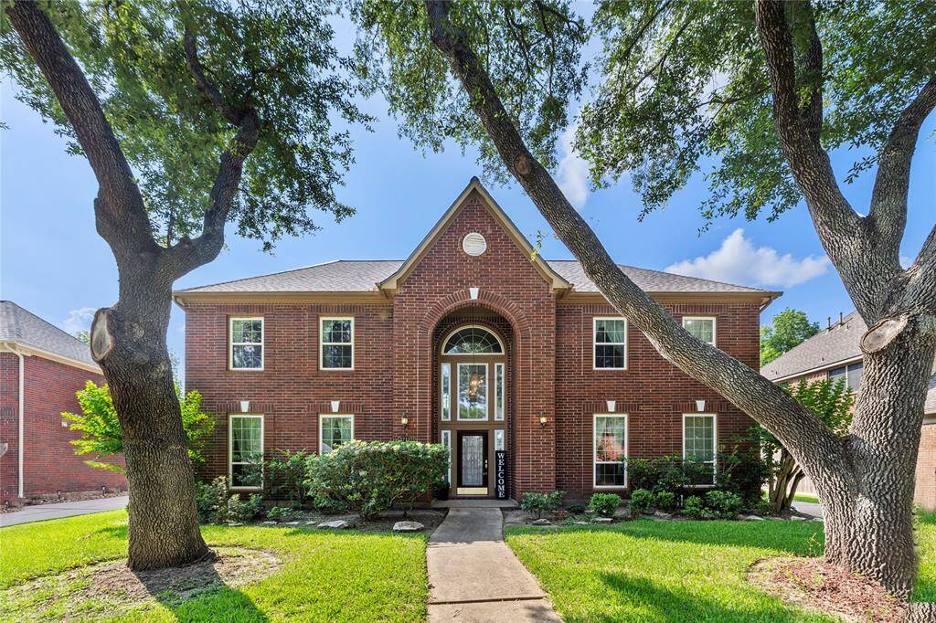 This photo showcases a charming two-story brick home with a symmetrical facade, framed by mature trees and a well-maintained lawn. The large windows and inviting entryway contribute to its welcoming curb appeal.