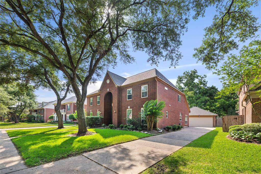 This photo showcases a charming two-story brick home with a well-maintained front yard, mature trees, and a long driveway leading to a detached garage.