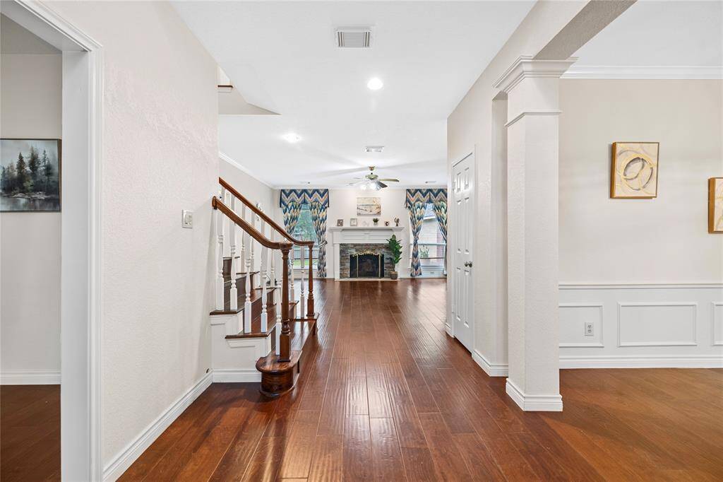 This photo showcases a bright, inviting entryway with elegant wood floors, leading to a cozy living area with a fireplace. The space features tasteful moldings and a staircase with wooden railings, creating a warm and welcoming ambiance.