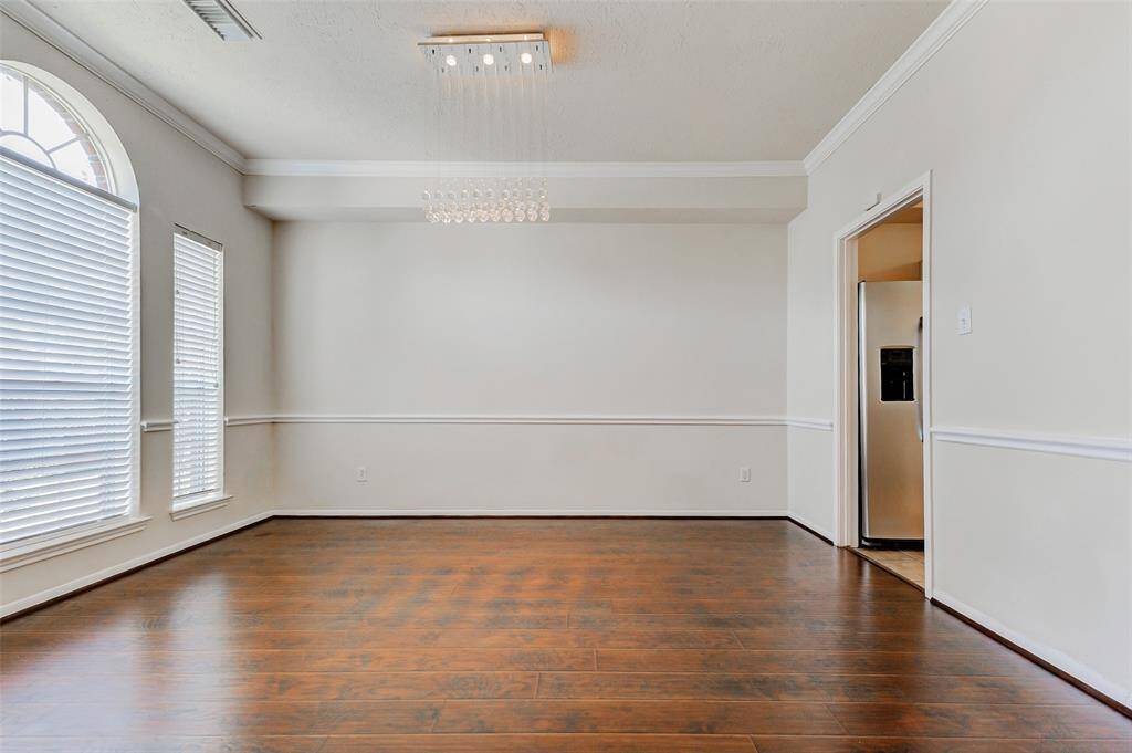 The formal dining room exudes timeless elegance, featuring gleaming laminate wood floors, crown molding, and chair-rail molding that add a refined architectural touch. Large windows allow for an abundance of natural light, creating a bright and inviting atmosphere—perfect for hosting dinners or special occasions.