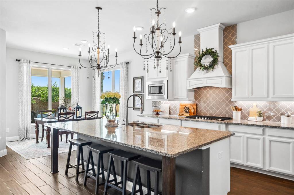 Gorgeous kitchen with stunning French chandeliers over a huge center island and designer range hood includes a 36" 5-burner cooktop and double wall ovens. Notice the undercabinet lighting, upgraded cabinets and trim, and wide open views to the pool and patio.