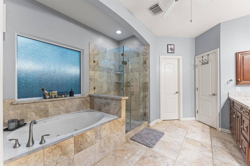 Primary bathroom with oversized soaking jacuzzi tip.  Seamless glass enclosure for the shower.  Double closets.