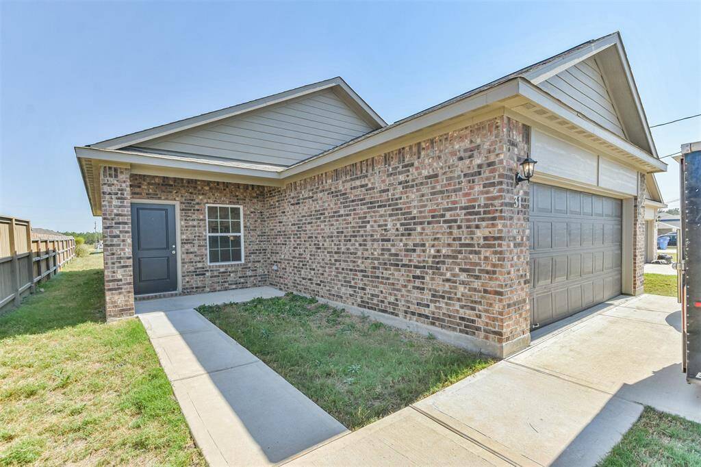 A charming brick home with a modern exterior, featuring a two-car garage and a neat pathway leading to the front door. Ideal for those seeking a low-maintenance yard and a welcoming entrance.
