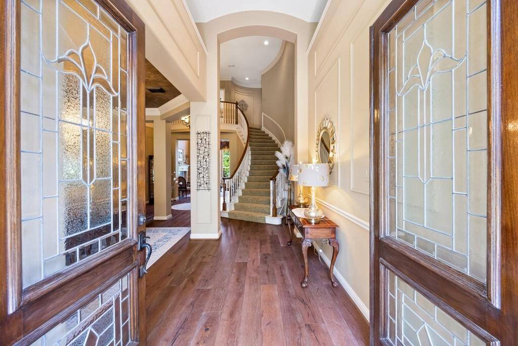 Double leaded-glass doors open to a soaring two-story foyer featuring rich hardwood flooring, custom millwork, and a sweeping staircase—setting the tone for elegance and sophistication throughout the home.