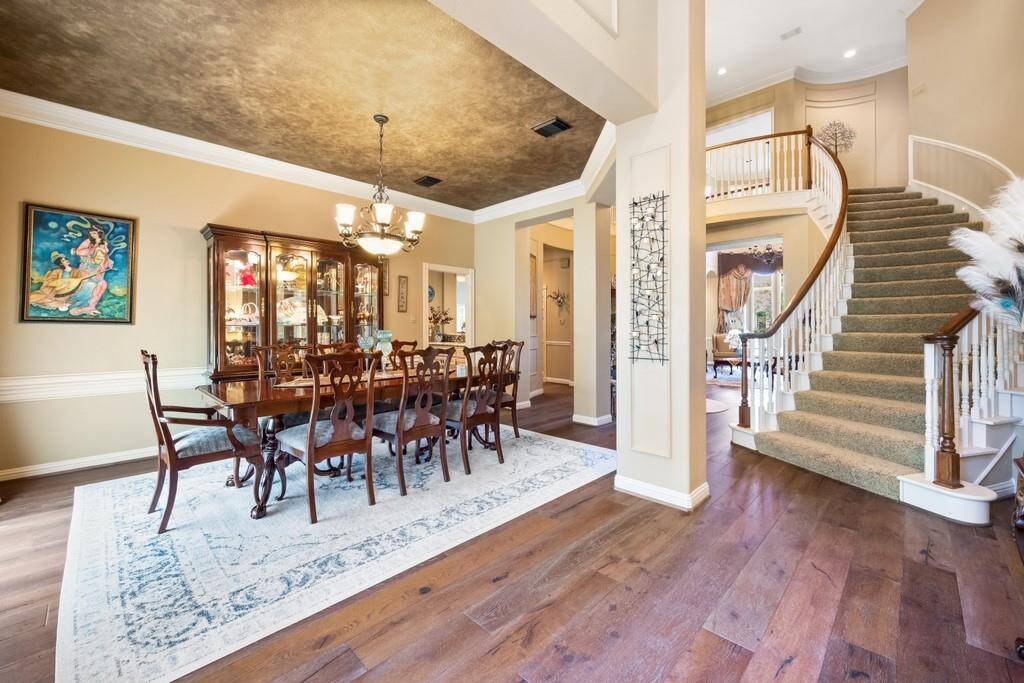 An open formal dining room flows seamlessly into the grand foyer, highlighted by a dramatic curved staircase, crown molding, and designer ceiling—ideal for elegant gatherings and memorable entertaining.