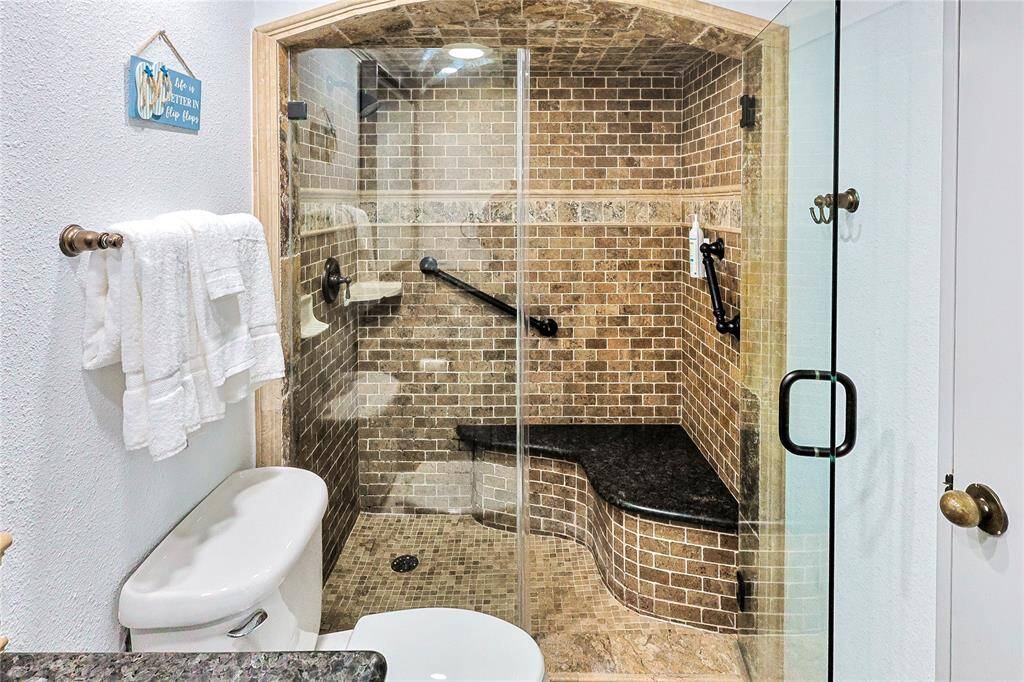 This bathroom features a warm, elegant design with a beautiful vanity and granite countertop. It includes a large mirror, modern fixtures, and a walk-in shower with stylish tile work and glass doors.