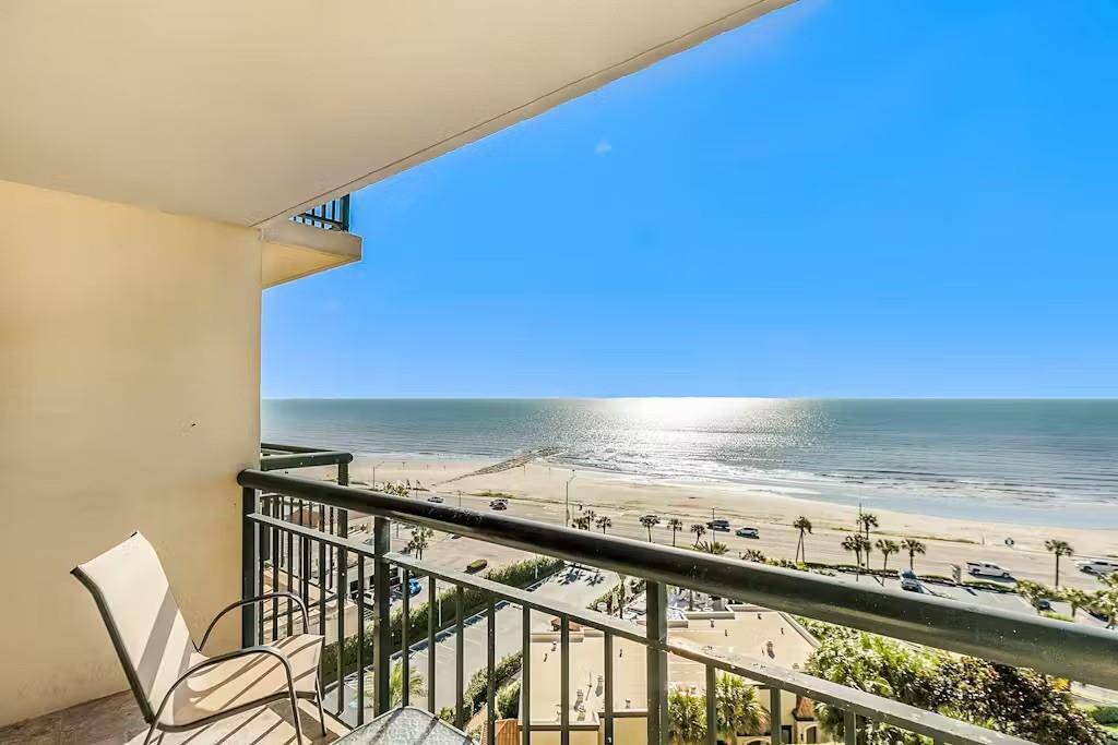 This photo showcases a stunning beachfront view from the balcony, featuring a clear blue sky and sparkling ocean. The balcony has seating, offering a perfect spot for relaxation and enjoying the scenic coastal landscape.  This shows how close you are to putting your toes in the sand!