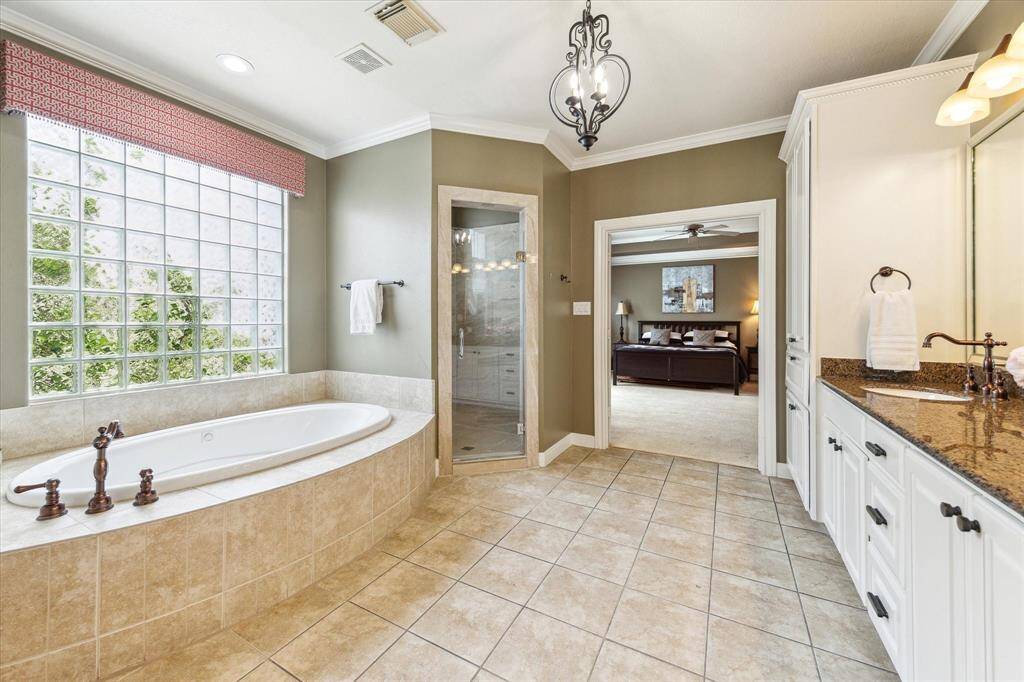 Double doors open to the light-filled primary bath with spa tub, walk-in shower, double sinks, and private commode room.