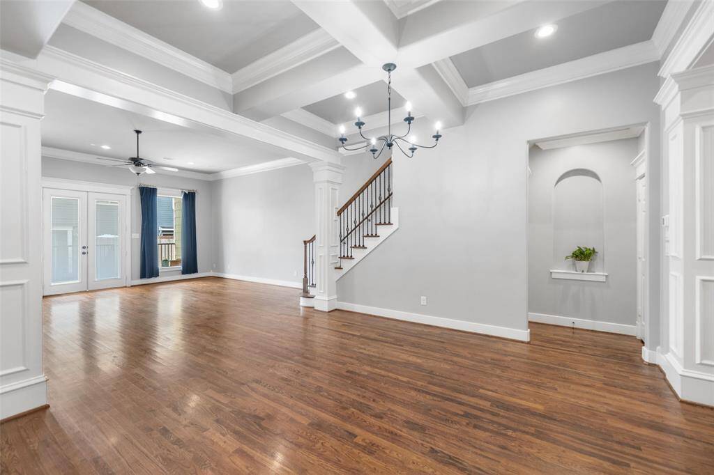 This spacious living area features elegant hardwood floors, coffered ceilings, and ample natural light. It includes a stylish chandelier, a cozy nook, and access to a patio through French doors, creating a perfect blend of sophistication and comfort.