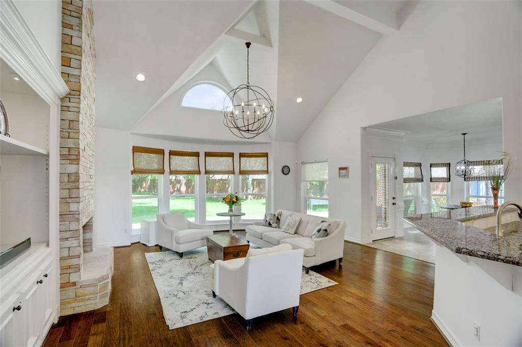 This is the view of the living area from the open foyer and features high vaulted ceilings, abundant natural light from large windows across the back and a cozy stone fireplace with built-ins.  The modern chandelier adds a touch of sophistication, creating a perfect space for entertaining.