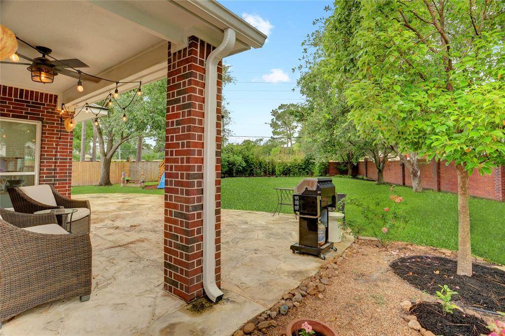 Discover the inviting covered patio, framed by a brick privacy fence, overlooking a lush, expansive backyard.
