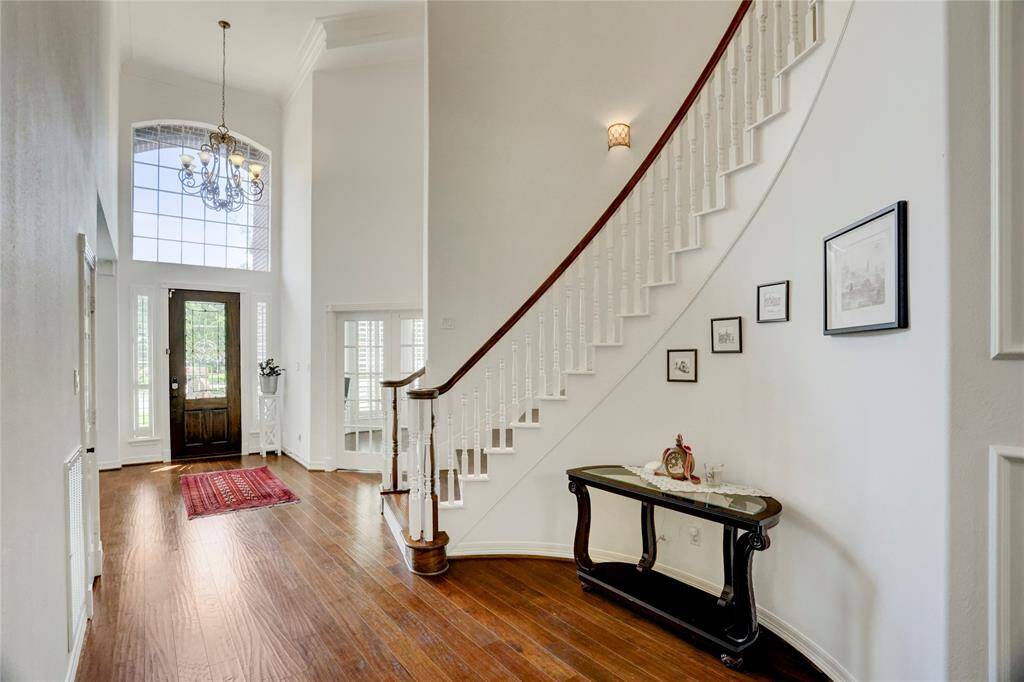 This photo showcases an elegant foyer with a high ceiling, large windows, and a grand staircase. The space features hardwood floors, a decorative chandelier, and a welcoming entrance