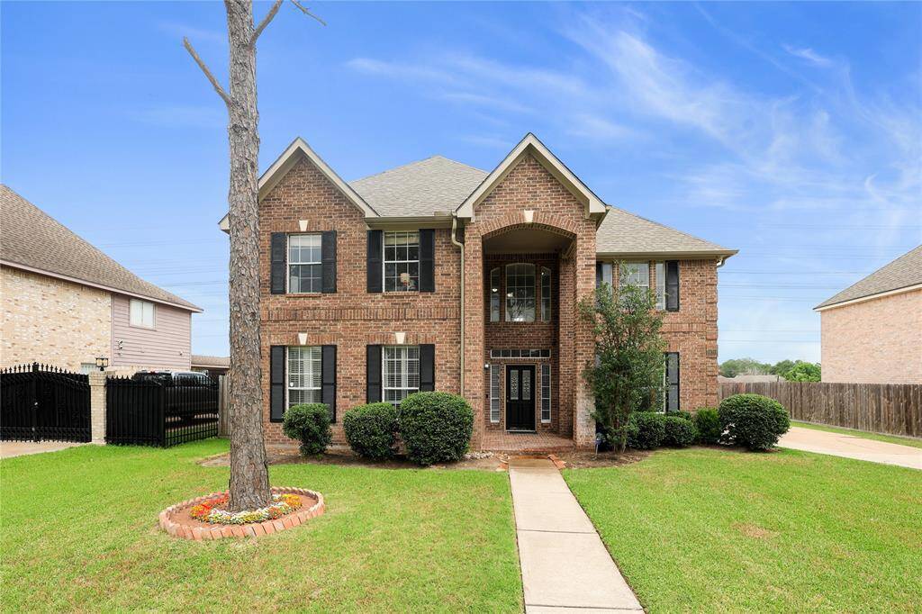 This two-story brick home features a classic design with a gabled roof and black shutters. The well-maintained front yard includes a walkway, manicured bushes, and a tree, creating an inviting curb appeal.